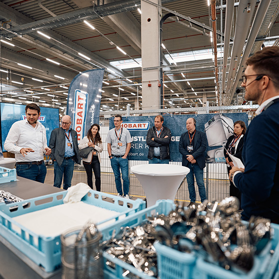 Präsentation von HOBART Komponenten in einem industriellen Umfeld mit Teilnehmern und blauen Sortierboxen