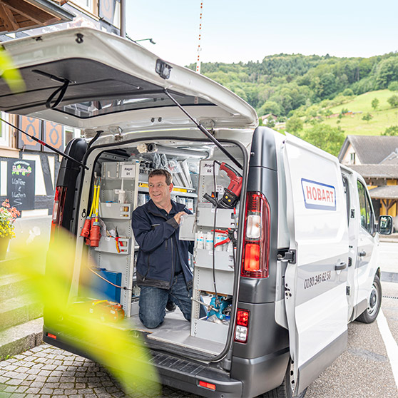 Servicefahrzeug mit HOBART-Logo und geöffneten Türen, ausgestattet mit Werkzeugen und Regalen für Außeneinsätze.