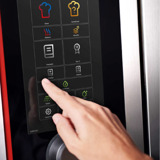 Nahaufnahme eines Fingers, der ein Touchscreen-Menü mit verschiedenen Funktionssymbolen wie Garen, CombiGuide, Retherm, MenuPlus, Protokolle, Einstellungen und Reinigung bedient.