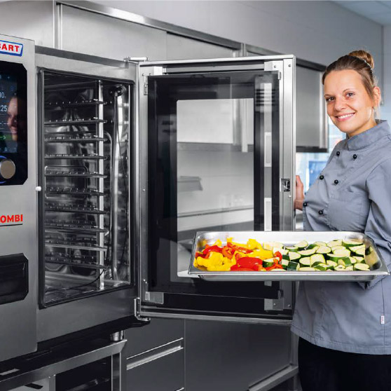Eine Person in Kochjacke hält ein Blech mit geschnittenem Gemüse wie Paprika und Zucchini vor einem geöffneten CHEF'S COMBI Ofen mit mehreren Einschüben und digitalem Bedienfeld.
