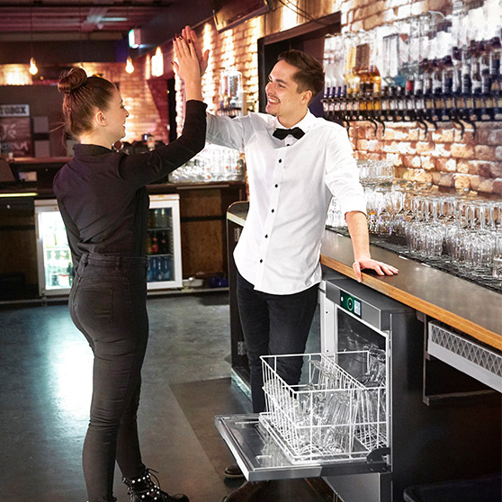 Zwei Mitarbeiter geben sich ein High-Five in der Restaurantküche neben einer HOBART GläserspülmaschineZwei Mitarbeiter geben sich ein High-Five in der Restaurantküche neben einer HOBART Gläserspülmaschine