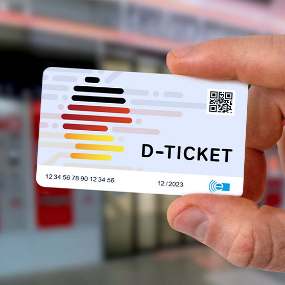 Nahaufnahme einer Hand, die ein Deutschlandticket (D-Ticket) hält. Die Karte zeigt ein modernes Design mit den Farben Schwarz, Rot und Gelb, QR-Code, Seriennummer und Gültigkeitsdatum „12/2023“. Ideal für bundesweite Fahrten im Nahverkehr.