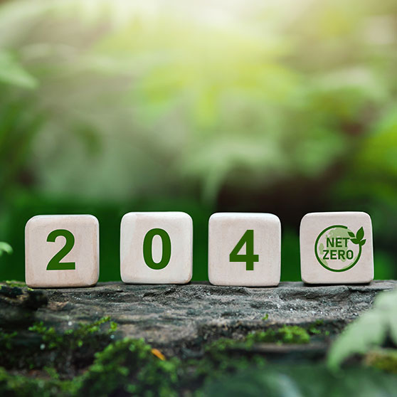 Holzblöcke mit der Aufschrift „2040“ und einem Net-Zero-Symbol auf Naturhintergrund. Symbol für Klimaneutralität und Nachhaltigkeit bis 2040.