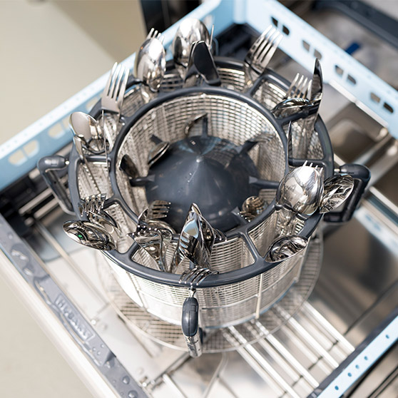 Besteckkorb mit sauberem Edelstahlbesteck wie Gabeln, Messern und Löffeln in einer professionellen Spülmaschine. Der Korb ist rund und sorgt für geordnete Platzierung des Bestecks.