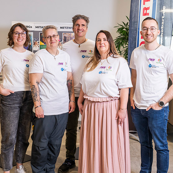 Gruppe von fünf Personen in T-Shirts von ITW – Teamfoto in einem Büro mit Banner und Poster im Hintergrund.