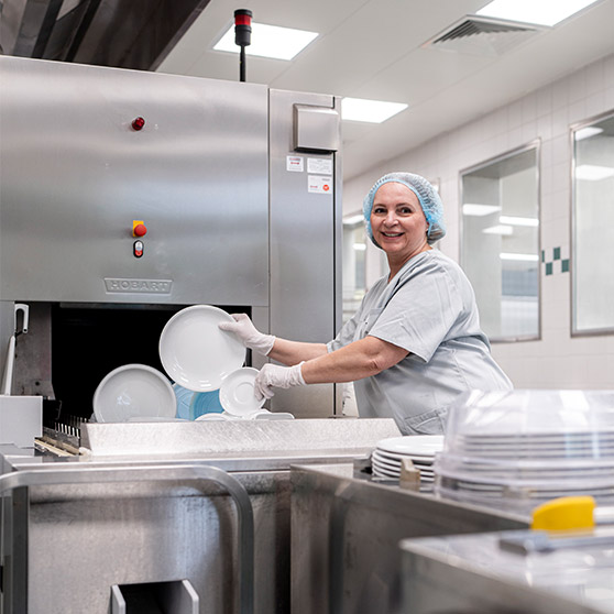 Bild zeigt eine HOBART Bandspülmaschine in einer professionellen Großküche, während Geschirr in die Maschine eingelegt wird. Ideal für Gastronomie und Kantinen, hohe Spülleistung, energieeffiziente Technologie und hygienische Reinigung großer Mengen Geschirr.