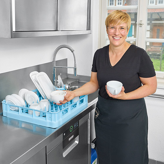 Bild zeigt eine HOBART Gläserspülmaschine in einer professionellen Küche mit einem blauen Geschirrkorb voller Gläser, Tassen und Teller. Ideal für Gastronomie und Hotellerie, kompakte Bauweise, energieeffiziente Technologie und hygienische Reinigung von Gläsern und Geschirr.