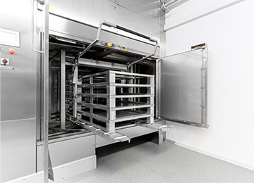 HOBART Palettenwaschanlage mit geöffneter Edelstahl-Waschkabine und flexiblem Reinigungswagen für Paletten und Behälter, ideal für industrielle Anwendungen in Hygienebereichen wie Lebensmittelproduktion und Pharma.