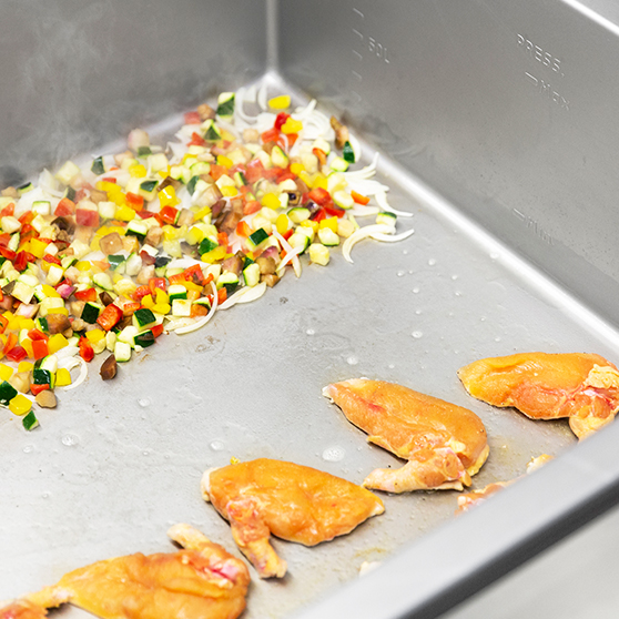 Innenraum einer HOBART Precipan mit bunt gewürfeltem Gemüse und angebratenem Geflügel, multifunktionales Gartechnik-Gerät für professionelle Küchen.