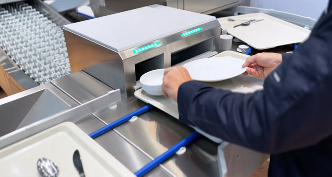 Nahaufnahme des HOBART SMART LOAD Beladungssystems mit ergonomischer Einlegung von Tellern und Schalen auf einem Tablett in die vorgesehenen Öffnungen für automatisierte Weiterverarbeitung in der professionellen Spülstraße.