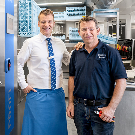 HOBART Servicetechniker steht in einer professionellen Spülküche neben einem zufriedenen Kunden, vor einer HOBART PROFI Spülmaschine, mit Werkzeug und Spülkörben im Hintergrund.