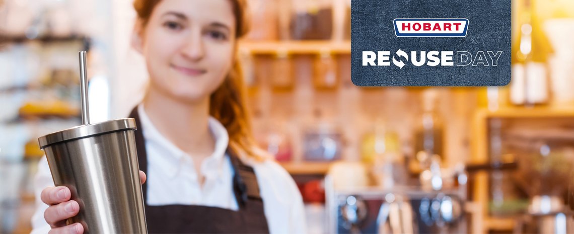 Eine Person hält einen wiederverwendbaren Edelstahlbecher mit Metallstrohhalm in einer Caféumgebung, daneben ein Schild mit dem HOBART Logo und der Aufschrift „REUSE DAY“.